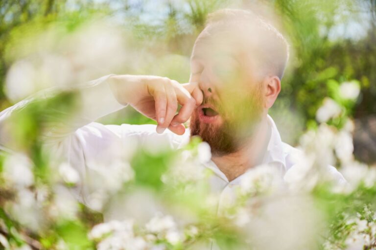 Man allergic suffering from seasonal allergy at spring in blossoming garden, sneezing.