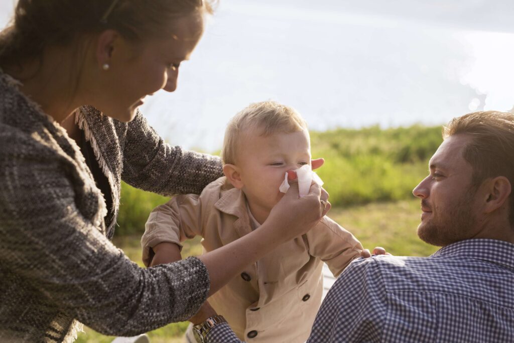 A family enjoying time outdoors while one member sneezes or uses tissues.