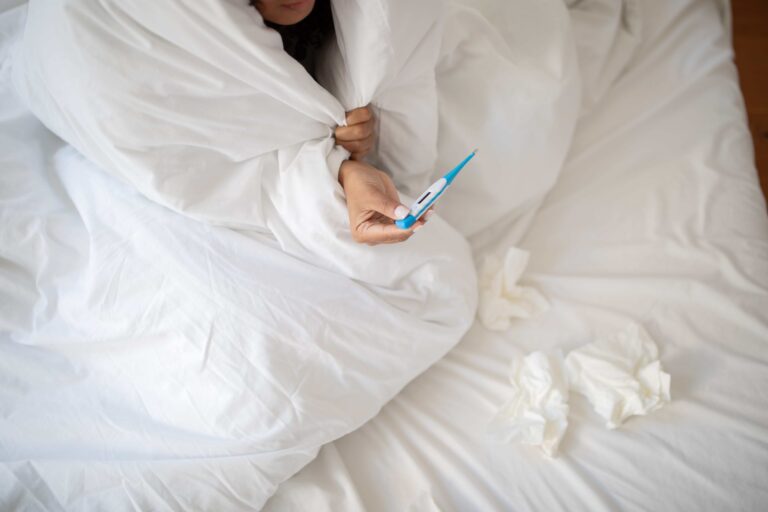 woman-with-fever-wrapped-in-white-blanket-holding