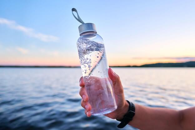 A man holds a bottle of water against the backdrop of a lake