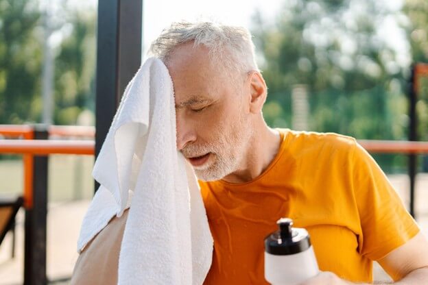 Senior man wiping sweat with towel after outdoor workout