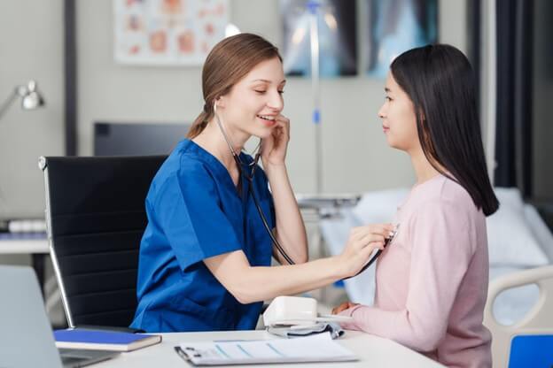 nurse uses a stethoscope on an patient to listen to his heart rate at desk