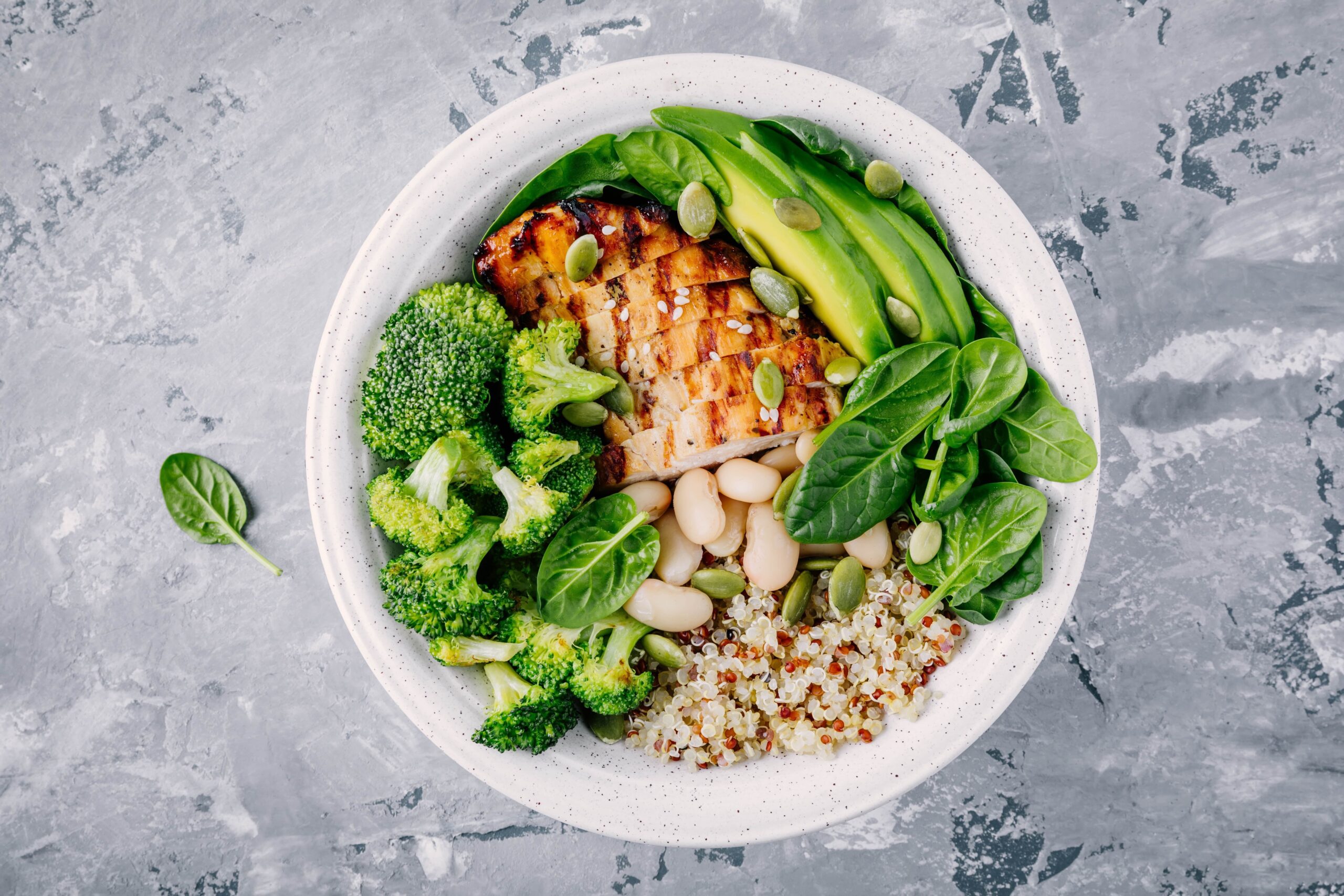 Green Buddha Bowl lunch with grilled chicken and quinoa, spinach, avocado, broccoli, and white beans