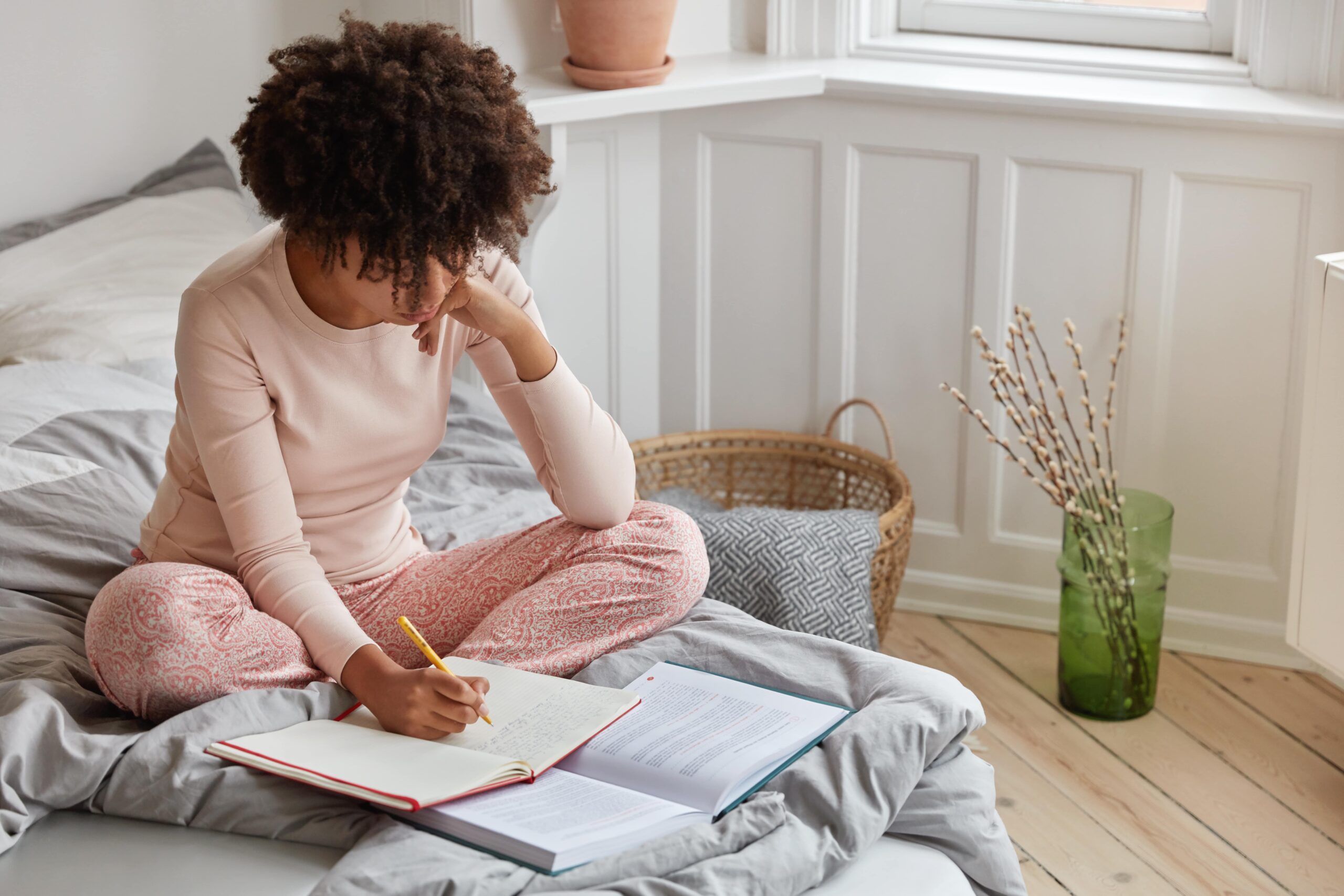 Top view of a busy dark-skinned woman writing down records in a notebook from a book.