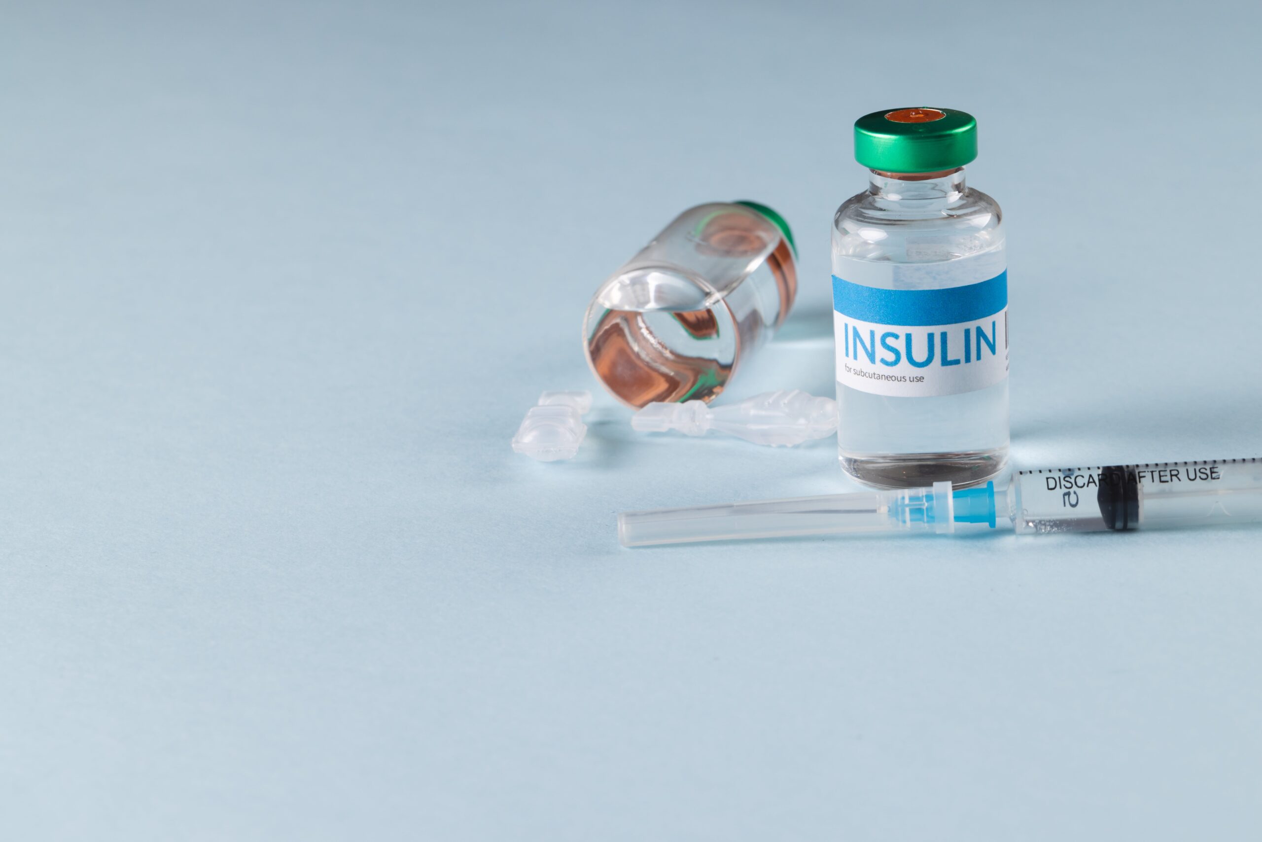 Vials of insulin with tablets and a syringe on a blue background with copy space