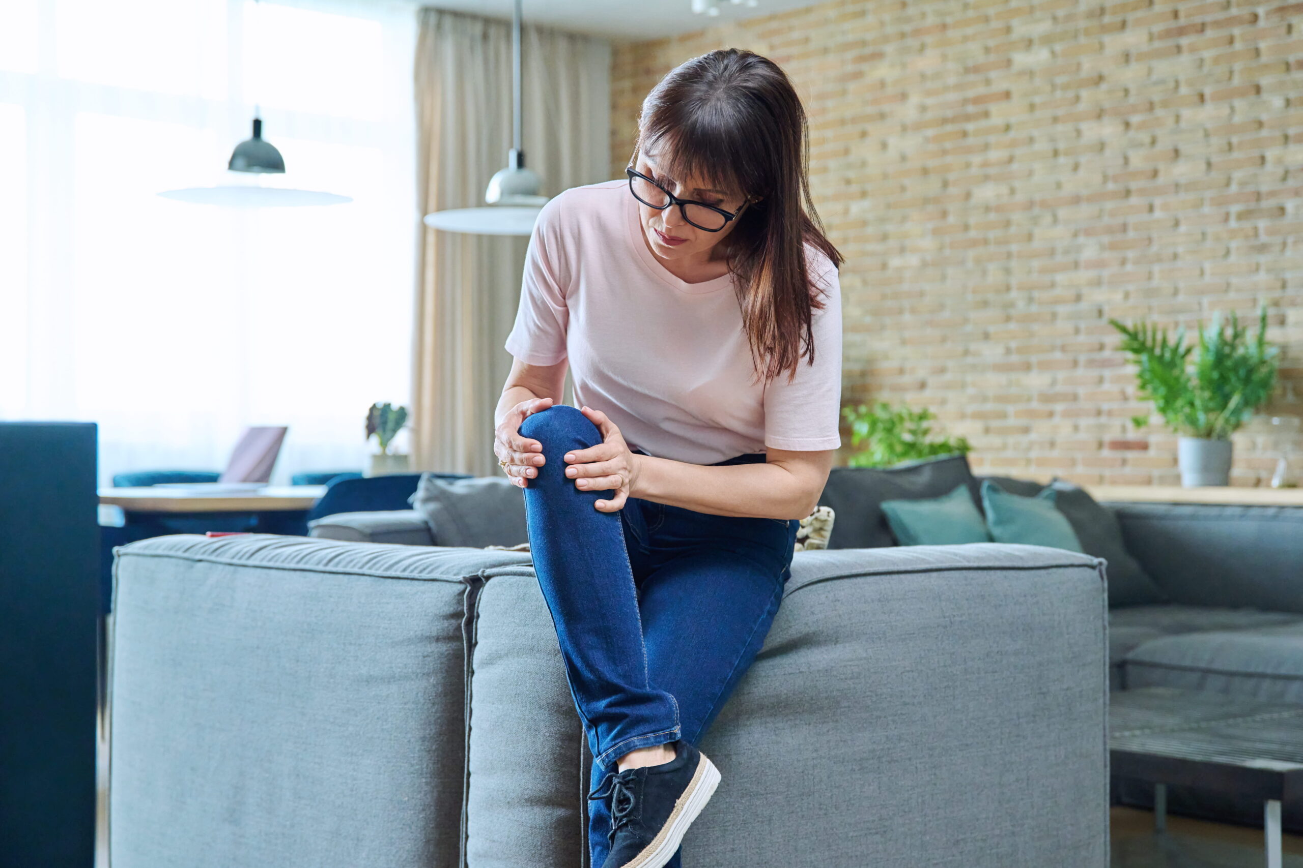 A middle-aged woman suffering from knee pain, at home in the living room.