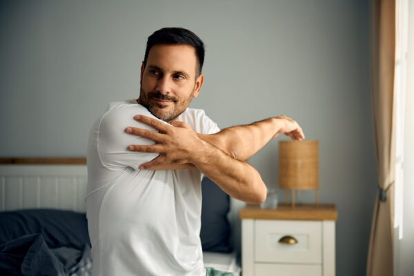 smiling-man-stretching-while-waking-up-in-bedroom