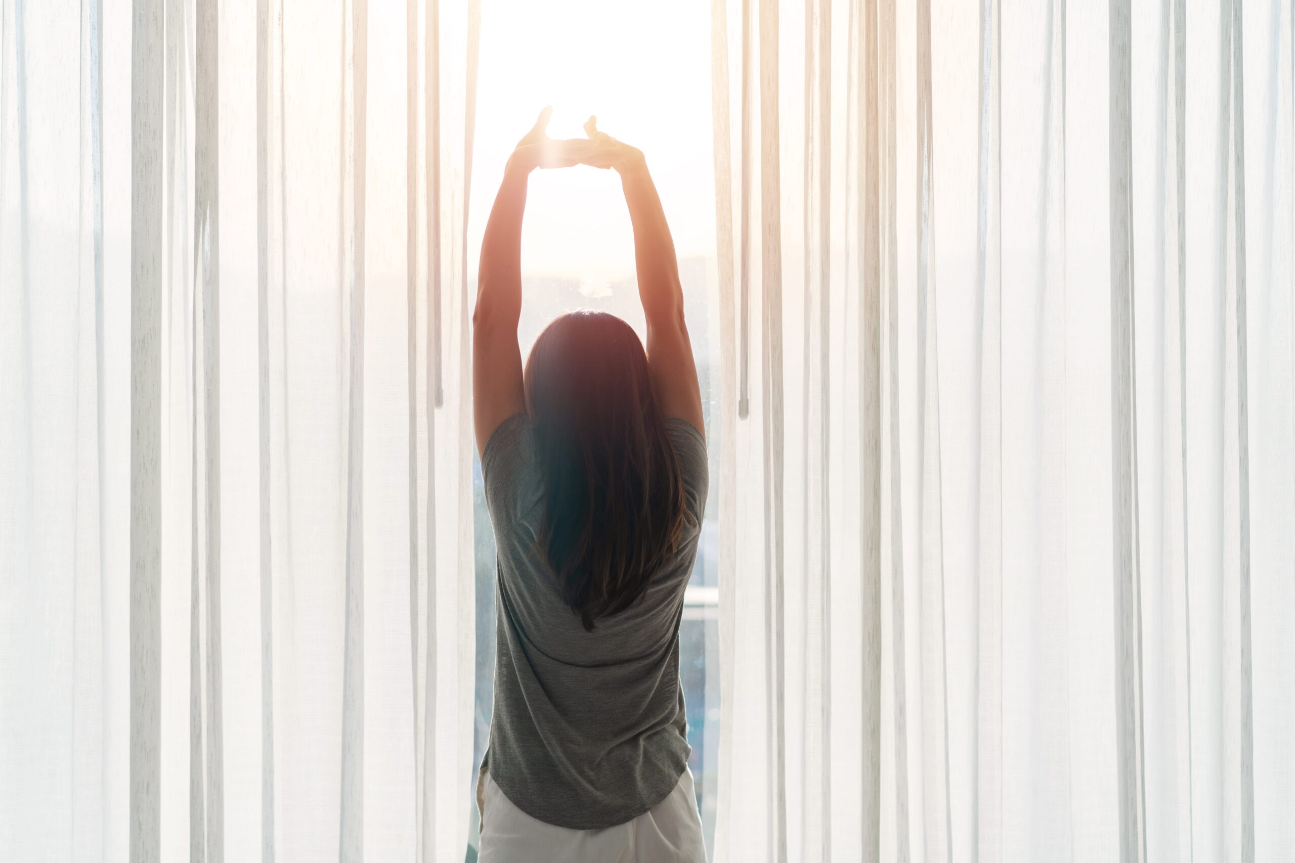An Asian woman sitting on the bed and stretching herself in the morning at home.