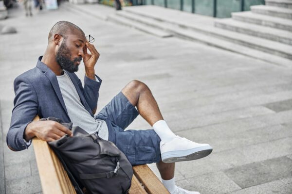 A man with headaches is sitting on a bench outdoors.