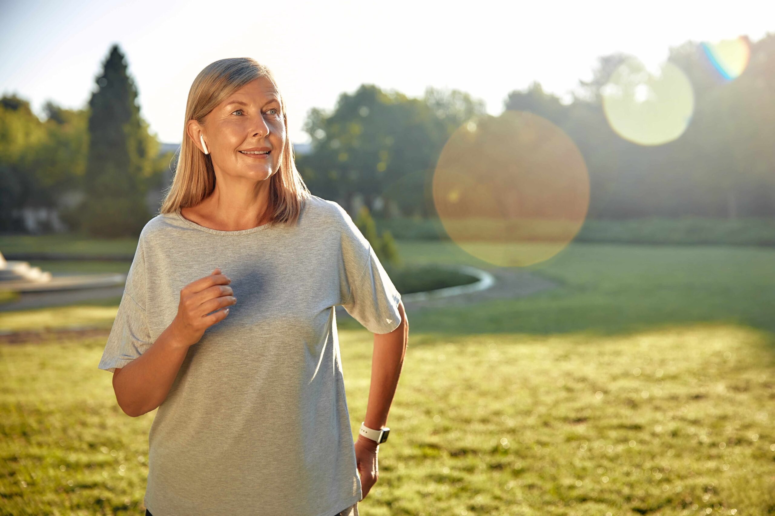 A joyful woman jogging outdoors in a sunny park.